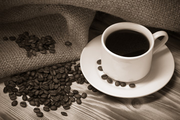 Coffee beans and coffee in white cup on wooden table with burlap
