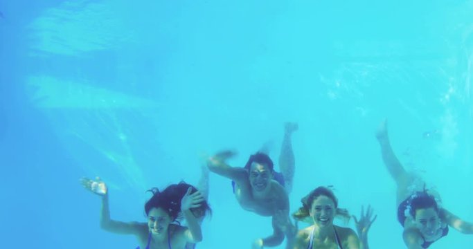 Four friends jumping into swimming pool and waving on their holidays