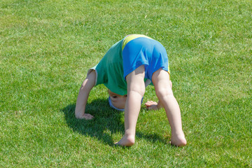 Fototapeta na wymiar Happy curly barefoot little boy on summer green grass
