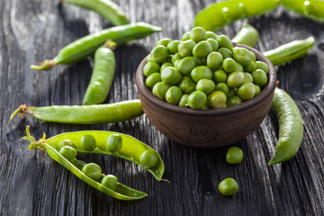 green peas in the pod on a black wooden table.