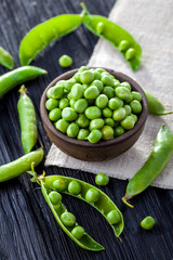 green peas in the pod on a black wooden table.