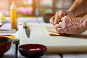 Man's hands holding bamboo mat. Cooking board on wooden surface. Preparation of futomaki sushi. Food is almost ready.