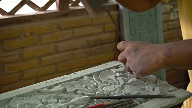 Cambodian artisan, chipping intricate, ornate details into a stone slab using a traditional hand chisel and mallet in his Siem Reap workshop. UHD video