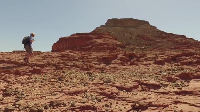 Woman climber conquers the desert and mountains.Girl with a backpack walking along the stone red desert. Steady shot