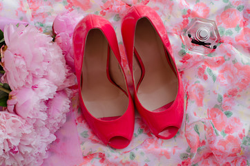 Obraz na płótnie Canvas Pink high heel shoes, women's perfume and bouquet of peonies on the background of a light fabric in flower