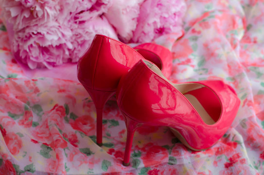 Pink high heels shoes and a bouquet of peonies on thin material with flower pattern