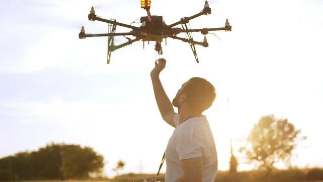 Young man controling drone in field at sunset. Slow motion Close up.