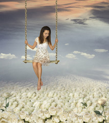 A girl is swinging. There is a beautiful sea of white roses under her.