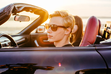 young happy couple in cabriolet in sunset light