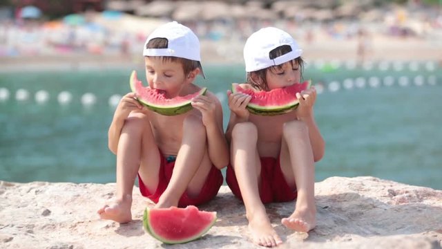 Two little children, boys brothers, eating watermelon on the beach, summertime