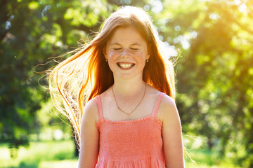 Portrait of smiling redhead girl with freckles in summer sun