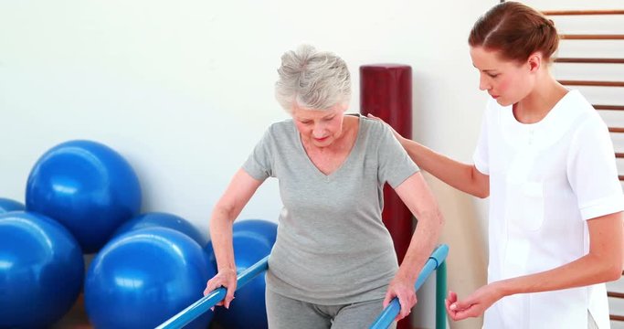 Smiling physical therapist helping patient walk with parallel bars