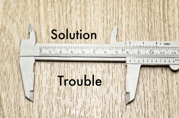 Business motivation and finance concept, vernier caliper with word SOLUTION vs TROUBLE over wooden...