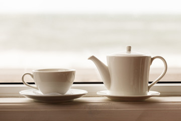 white teacup and teapot on the windowsill. Soft focus.
