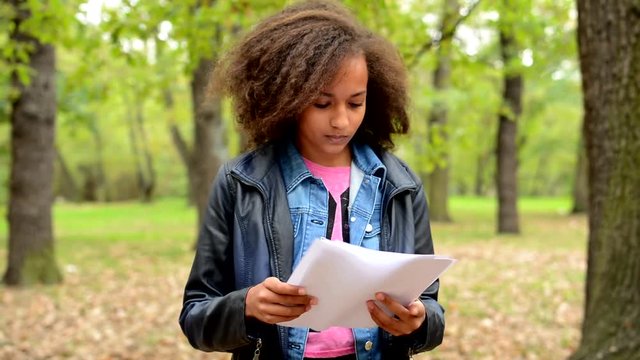 young african upset girl hold papers and read it in the park - contents is unclear 