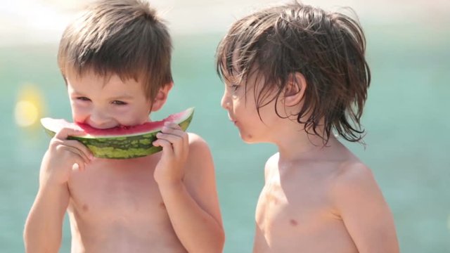 Two little children, boys brothers, eating watermelon on the beach, summertime