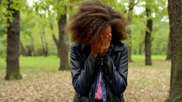 young sad african girl cry and cover her face with hands in the forest - miserable