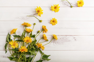 Yellow daisy flowers on light wooden background. High top view.