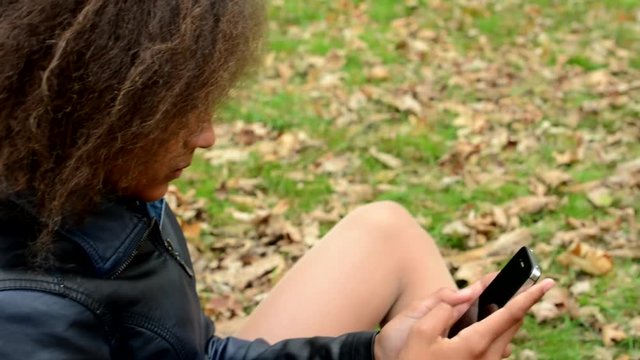 young charming african girl work with smartphone in the forest - dry leaves on the grass - close up