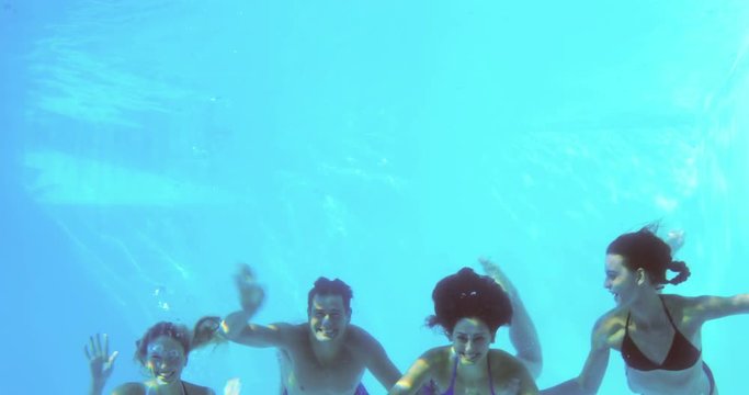 Four friends jumping into swimming pool and waving on their holidays