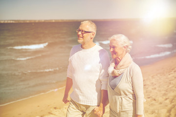 happy senior couple walking along summer beach