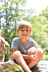 Portrait of cute little boy sitting on rock by river © goodluz