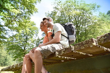 Couple of hikers sitting on a bridge looking at river water