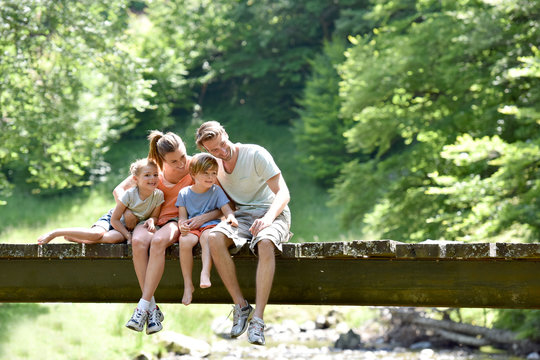 Family sitting on a bridge looking at fish in river