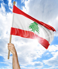 Person's hand holding the Lebanese national flag and waving it in the sky, 3D rendering