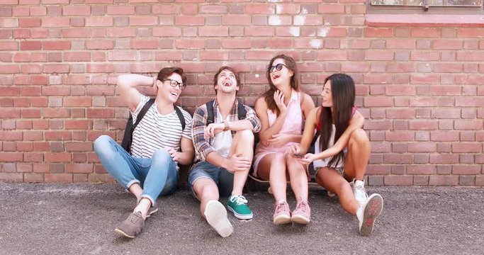 Hip friends using smartphone sitting against wall