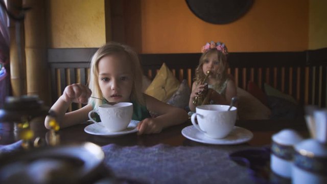 Two cute little blonde girls are having tea in a cafe