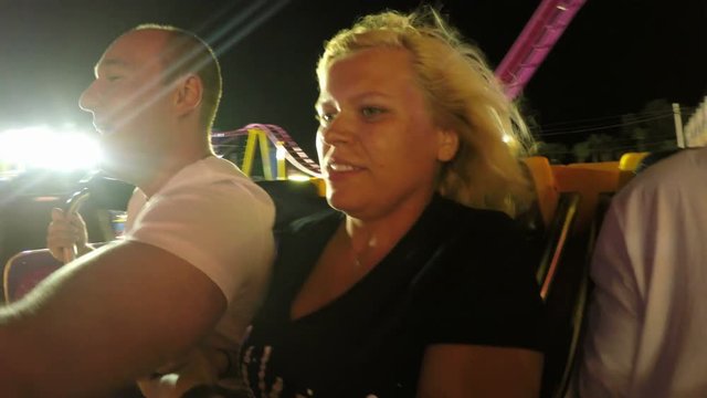 Happy couple having fun on the roller coaster ride in the amusement park at night.