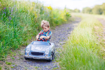Little kid boy driving big toy car with a bear, outdoors.