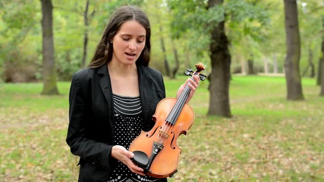 young happy attractive woman describe parts of violin in the forest - she point pieces of violin and talk about them