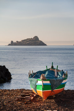 Mediterranean seascape: fishing boat near Acitrezza, Sicily, and a sea lava stack in the distance