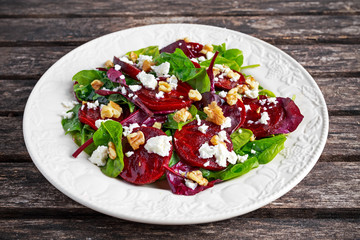 Healthy Beet Salad with fresh sweet baby spinach, kale lettuce, nuts, feta cheese on wooden table.