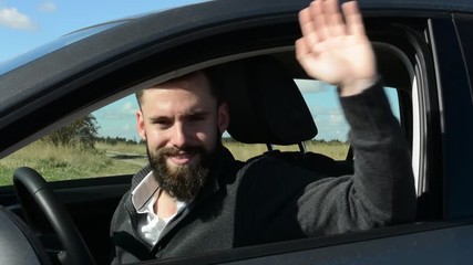 young handsome hipster man sits in the car and waves with one hand (welcome) - countryside - sunny weather 