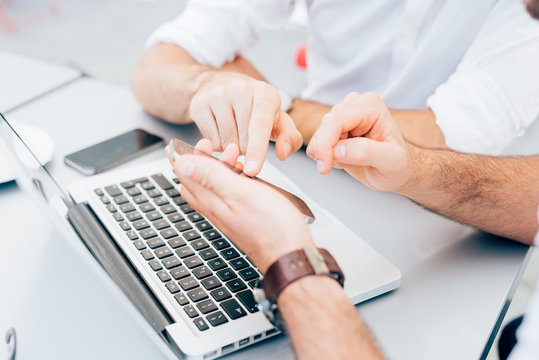 Close up on the hands of two men using technological devices, tapping the screen of a tablet hand hold - technology, communication, multitasking concept