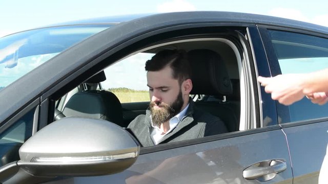 young handsome hipster man sits in the new car and signs a contract to sell the car and gets key from seller - countryside