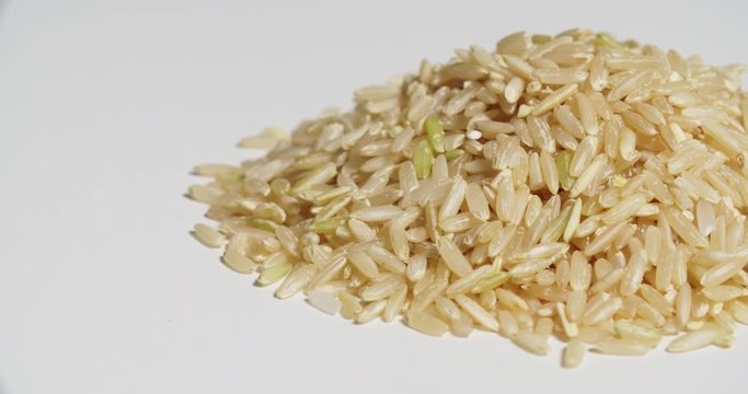 Brown Rice Pile Uncooked Spinning on White. Left side of a pile of uncooked brown rice spins right on white
