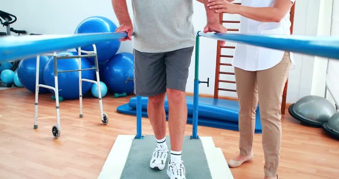 Physiotherapist helping patient walk with parallel bars