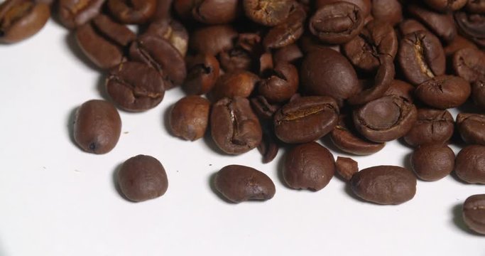 Coffee Beans Above Pile Close Up Bottom Edge on White Spins. From above lower side of a pile of brown coffee beans spins right on white
