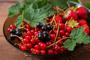 Plate with fresh berries (strawberries and currants) on dark wooden background