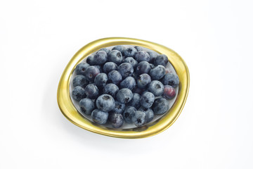 Group of bilberries placed on a golden dish with white isolated background