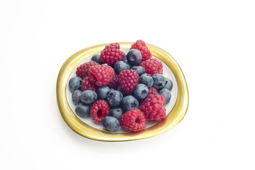 Group of raspberries and bilberries placed on a golden dish with white isolated background