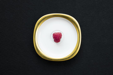 Raspberry placed on a golden white dish with isolated black background
