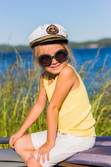 Portrait of a cheerful girl in sunglasses in a marine cap cabin boy on the lake on a sunny summer day. At the cap emblem of the Russian Navy.
