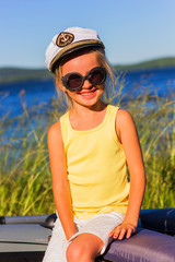 Portrait of a cheerful girl in sunglasses in a marine cap cabin boy on the lake on a sunny summer day. At the cap emblem of the Russian Navy.
