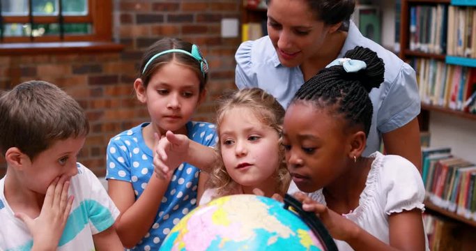 Pupils looking at the globe in library with their teacher in elementary school