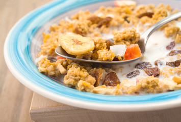 macro making spoon in bowl of cereal with fruit on wooden